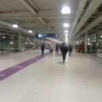 Pasillo amplio y luminoso del aeropuerto Jorge Chávez, con piso claro, una franja morada con dibujos de aviones y pasajeros caminando