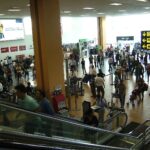 Pasajeros y familias en el hall del aeropuerto Jorge Chávez de Lima, con un coche de bebé y letreros de información.