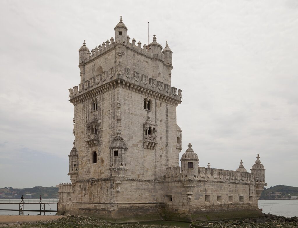 Lisboa desde Perú: la Torre de Belém, de piedra clara con torrecillas y almenas, a orillas del río bajo un cielo gris, con una pasarela a la izquierda
