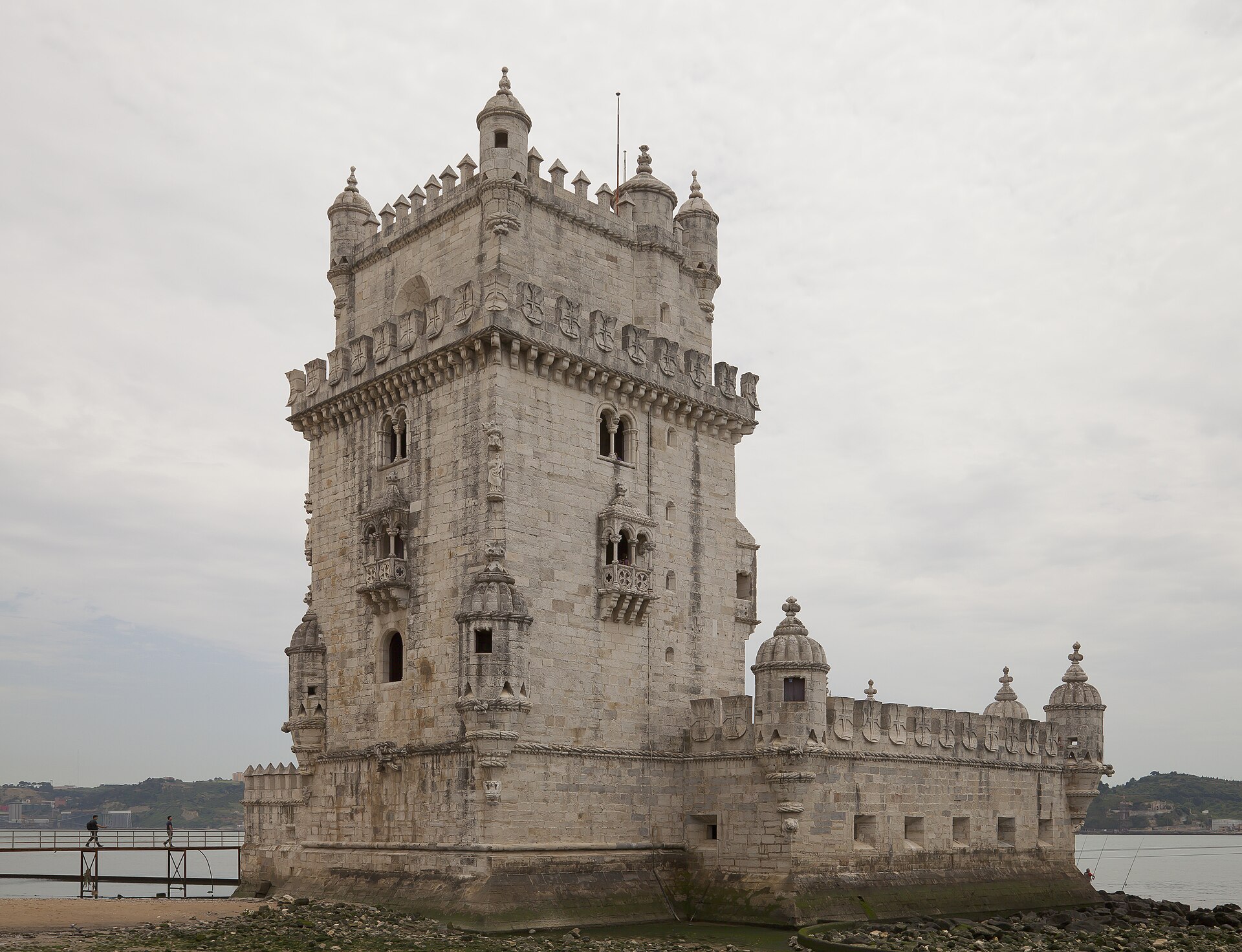 Lisboa desde Perú: la Torre de Belém, de piedra clara con torrecillas y almenas, a orillas del río bajo un cielo gris, con una pasarela a la izquierda