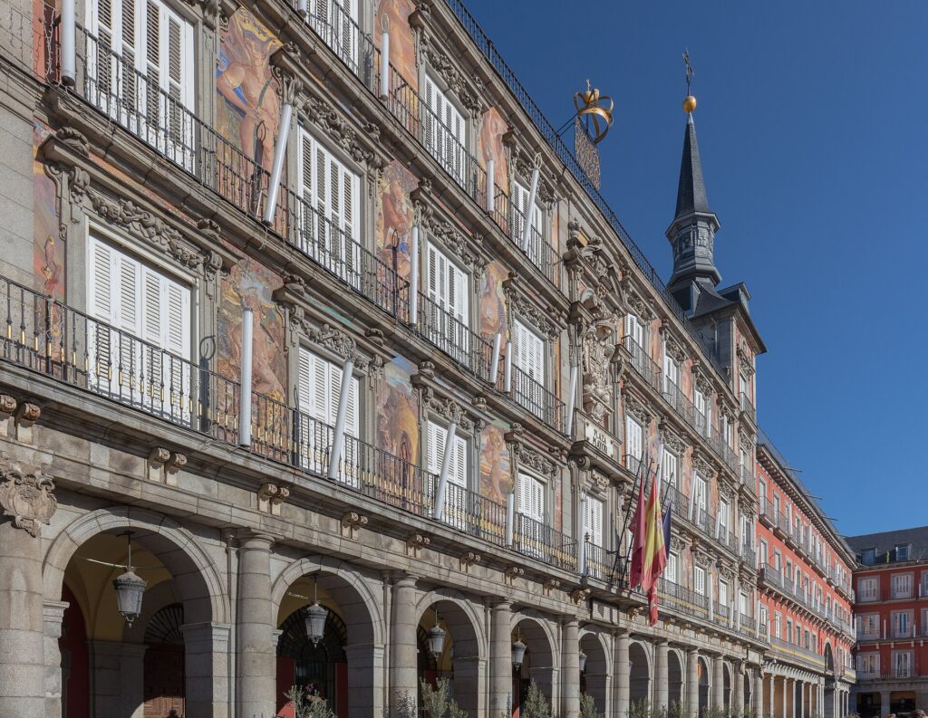 Madrid desde Perú: Casa de la Panadería en la Plaza Mayor, con frescos, balcones de hierro, torre con chapitel y banderas bajo cielo azul
