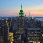 Nueva York desde Perú: rascacielos de Manhattan al atardecer con el Empire State iluminado de verde y el One World Trade Center al fondo
